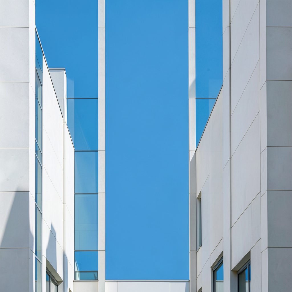 Wide photograph of a school campus with symmetrical architecture, soft sky-blue and off-white buildings framed by green hills, calm and orderly atmosphere